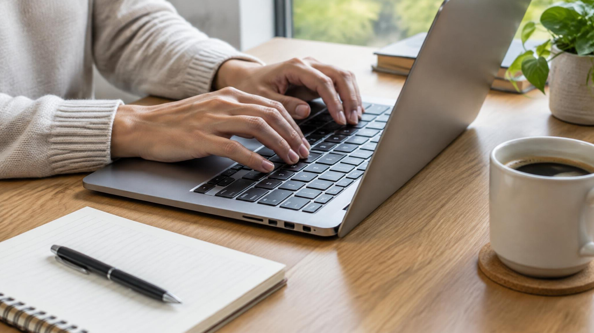 Hands typing on a laptop on a desk with notes